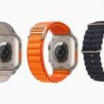 Three Apple Watch Ultra devices are shown from behind to feature their three different bands, including a gray-and-yellow Trail Loop, orange Alpine Loop, and black Ocean Band.  