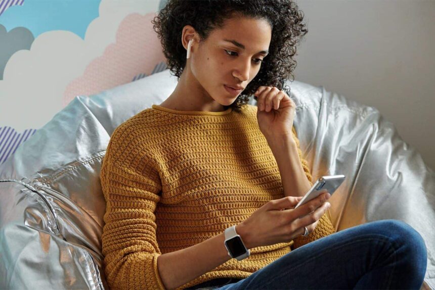 Woman on sofa holding iPhone listening to AirPods.  