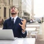 Man sits at a laptop outside looking up at the sky in distress  