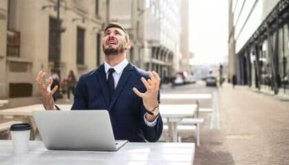 Man sits at a laptop outside looking up at the sky in distress  
