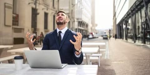 Man sits at a laptop outside looking up at the sky in distress