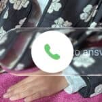 Hand rests on pink surface; phone icon and partial text overlay, floral pattern in the background.