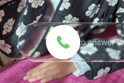 Hand rests on pink surface; phone icon and partial text overlay, floral pattern in the background.