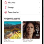 The Library screen showing a list of categories including Playlists, Artists, Albums, Songs, and Downloaded. The Recently Added heading appears below the list. The MiniPlayer showing the title of the current song and the Pause and Next buttons appear near the bottom.  