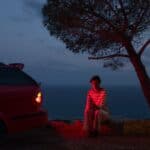 Remote location, person sitting next to the car, illuminated by taillights, holding an iPhone.