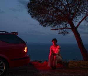 Remote location, person sitting next to the car, illuminated by taillights, holding an iPhone.
